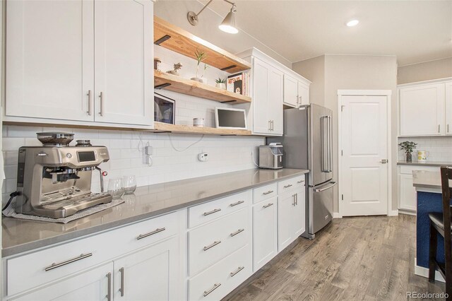 kitchen with wood finished floors, freestanding refrigerator, backsplash, and white cabinets