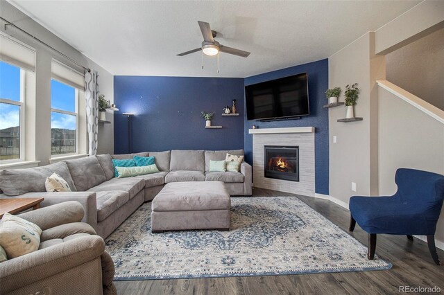 living area with a ceiling fan, baseboards, a tiled fireplace, and wood finished floors