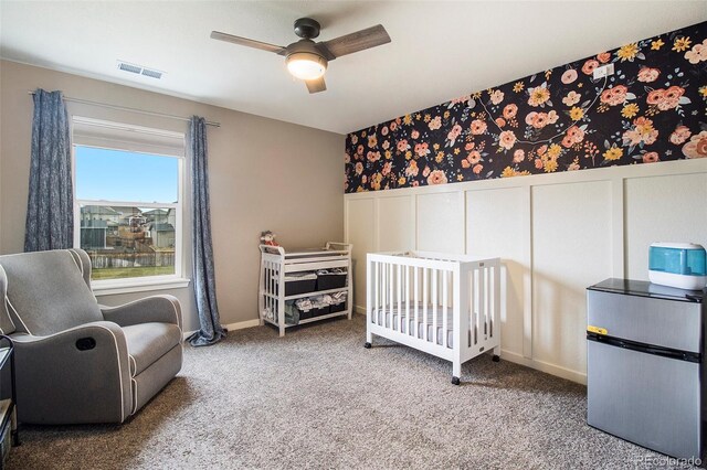 bedroom featuring a ceiling fan, visible vents, a decorative wall, a wainscoted wall, and carpet flooring