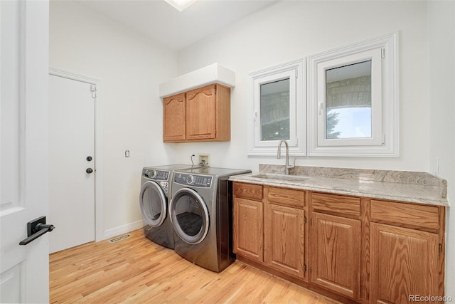 clothes washing area with light hardwood / wood-style floors, cabinets, washer and clothes dryer, and sink