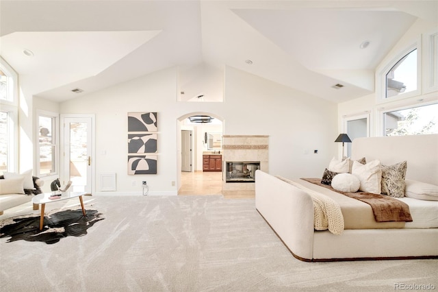 carpeted bedroom featuring multiple windows, a tiled fireplace, and high vaulted ceiling