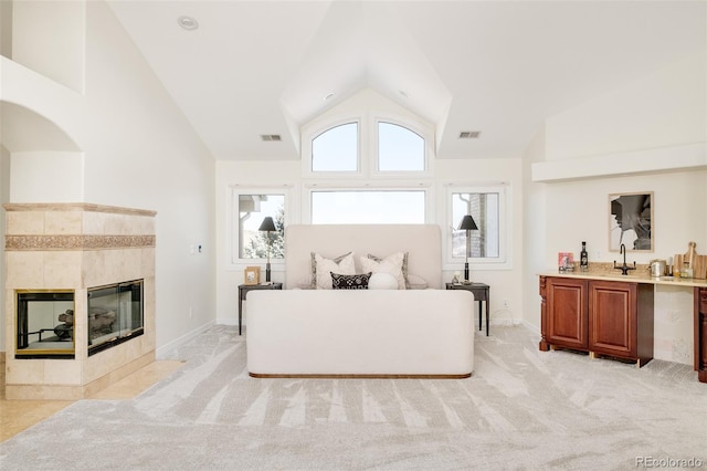 carpeted living room featuring a tiled fireplace and high vaulted ceiling