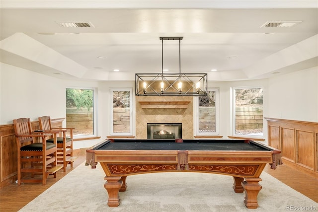 game room featuring a tray ceiling, a premium fireplace, and light wood-type flooring