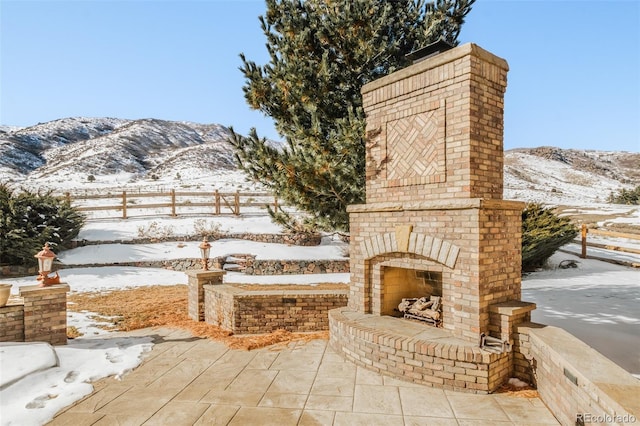 snow covered patio featuring an outdoor brick fireplace and a mountain view