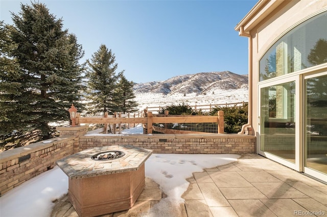 snow covered patio featuring a mountain view and a fire pit