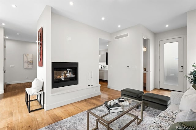 living room featuring recessed lighting, visible vents, wood finished floors, and a multi sided fireplace