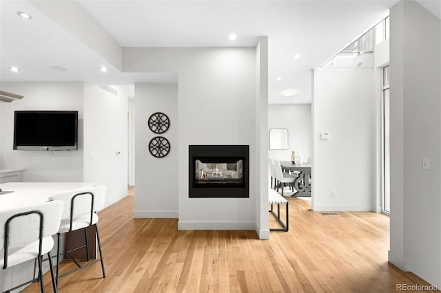 living room featuring light wood-type flooring, baseboards, a multi sided fireplace, and recessed lighting