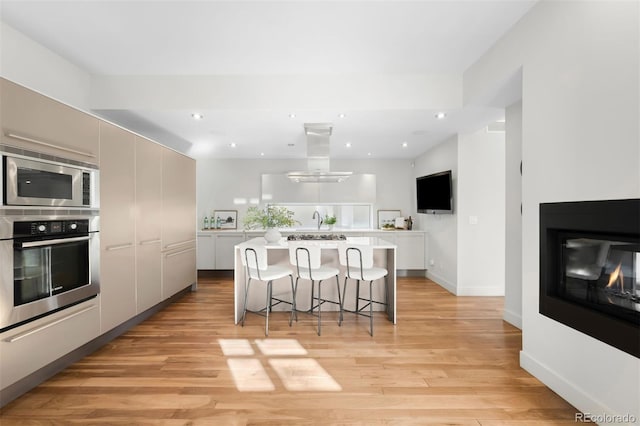 kitchen with island range hood, stainless steel appliances, light countertops, light wood-type flooring, and a kitchen bar