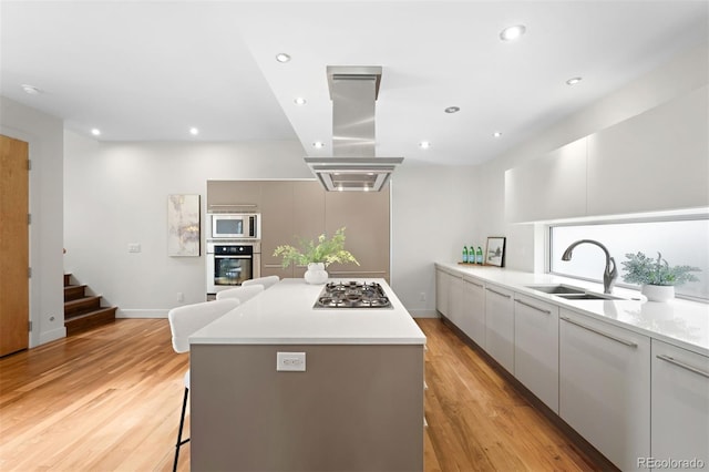 kitchen with island range hood, a kitchen island, modern cabinets, appliances with stainless steel finishes, and a sink