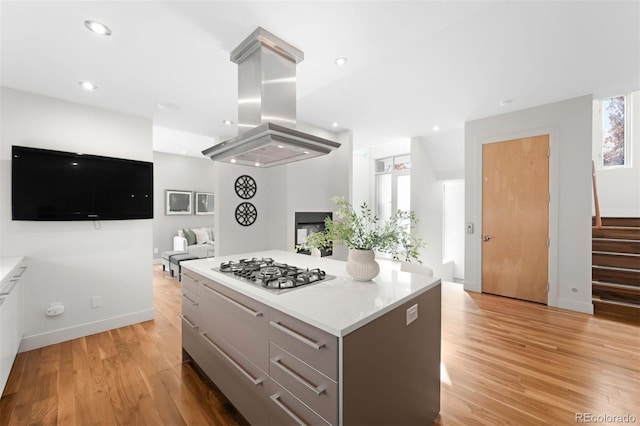 kitchen with island range hood, open floor plan, gray cabinetry, light wood-style floors, and stainless steel gas stovetop