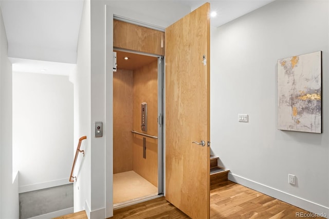 staircase with elevator, baseboards, and wood finished floors