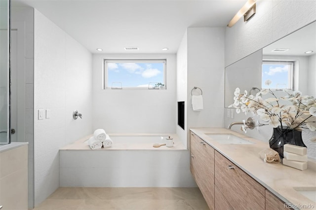 bathroom with visible vents, double vanity, a sink, and a bath