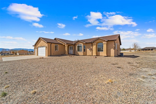single story home featuring a garage, driveway, stucco siding, and central AC unit