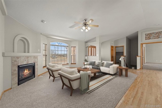 living area featuring vaulted ceiling, a tiled fireplace, a ceiling fan, wood finished floors, and baseboards