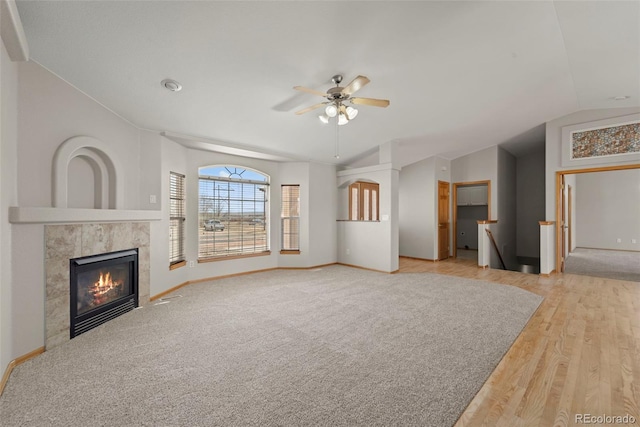 unfurnished living room with baseboards, a fireplace, wood finished floors, ceiling fan, and vaulted ceiling
