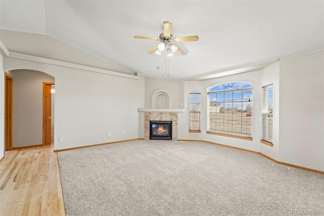 unfurnished living room featuring baseboards, a tiled fireplace, a ceiling fan, light carpet, and vaulted ceiling