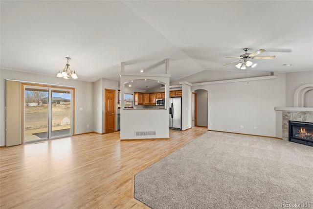 unfurnished living room featuring visible vents, a tile fireplace, lofted ceiling, light wood-type flooring, and ceiling fan with notable chandelier