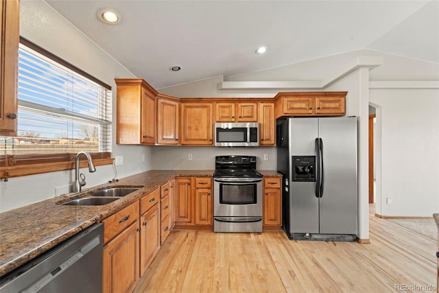 kitchen featuring lofted ceiling, light wood-type flooring, stainless steel appliances, dark stone counters, and a sink