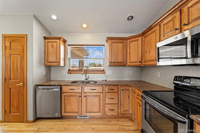 kitchen with stainless steel appliances, a sink, visible vents, light wood-style flooring, and brown cabinets