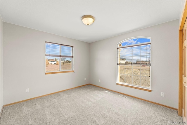 carpeted spare room featuring baseboards, a wealth of natural light, and visible vents