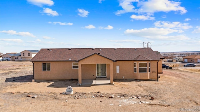 back of house featuring a shingled roof, stucco siding, and a patio