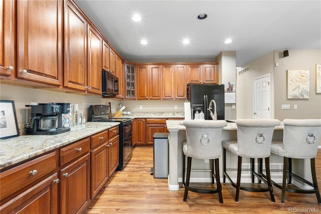 9631 S Dover Way, Littleton, CO 80127 - kitchen with black appliances, light wood-style floors, a breakfast bar area, brown cabinets, and recessed lighting