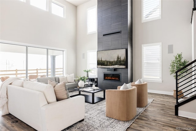 living room with wood-type flooring, a towering ceiling, a fireplace, and a wealth of natural light