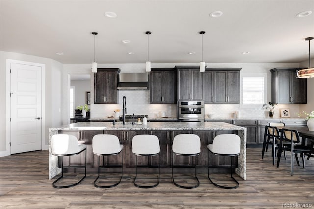 kitchen with a center island with sink, wall chimney exhaust hood, and hanging light fixtures