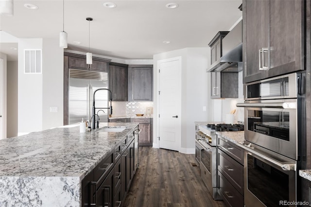 kitchen featuring light stone countertops, premium appliances, a center island with sink, and sink