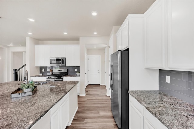 3325 Umber Cir, Castle Rock, CO 80109 - kitchen featuring stainless steel appliances, a sink, light wood-type flooring, decorative backsplash, and white cabinetry