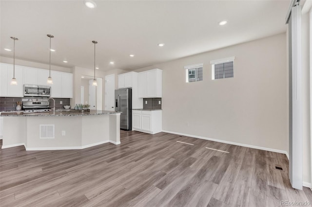 3325 Umber Cir, Castle Rock, CO 80109 - kitchen with appliances with stainless steel finishes, decorative backsplash, light wood-style floors, a center island with sink, and recessed lighting