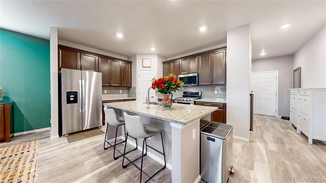 kitchen featuring stainless steel appliances, a kitchen breakfast bar, dark brown cabinets, and an island with sink