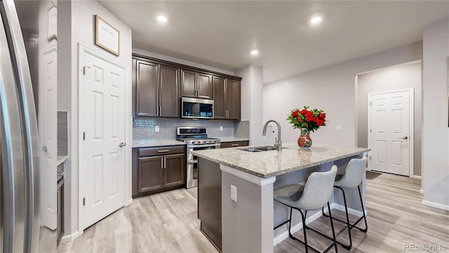 kitchen with light wood finished floors, backsplash, dark brown cabinetry, stainless steel appliances, and a sink