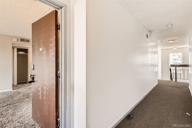 hallway with carpet, baseboards, and a textured ceiling