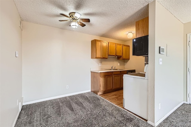 kitchen featuring washer / dryer, brown cabinetry, light colored carpet, black microwave, and a sink