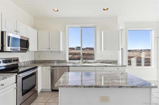 kitchen with light tile patterned flooring, white cabinets, light stone countertops, appliances with stainless steel finishes, and a kitchen island