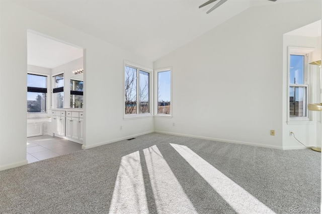 unfurnished living room with a healthy amount of sunlight, ceiling fan, light colored carpet, and vaulted ceiling