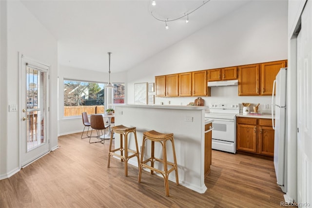 kitchen with white appliances, a kitchen breakfast bar, a center island, decorative light fixtures, and light wood-type flooring