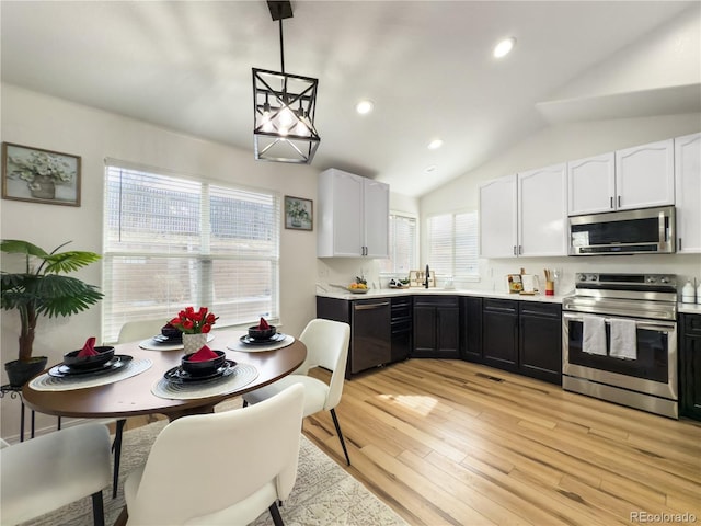 kitchen with appliances with stainless steel finishes, white cabinetry, lofted ceiling, hanging light fixtures, and light wood-type flooring