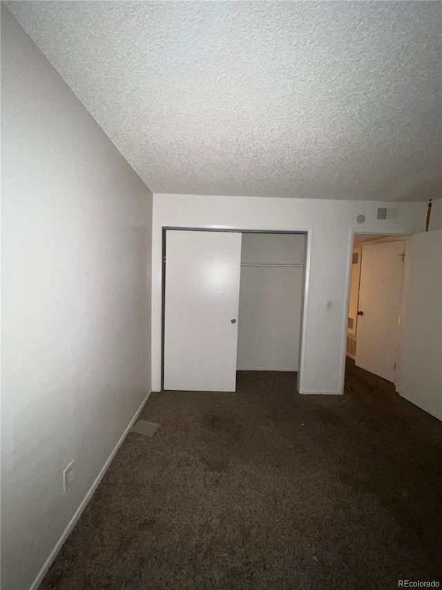 unfurnished bedroom with dark colored carpet, a closet, and a textured ceiling