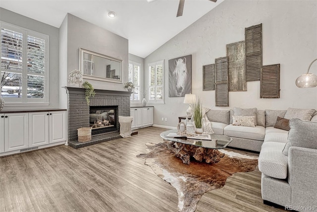 living room with ceiling fan, lofted ceiling, light hardwood / wood-style floors, and a brick fireplace