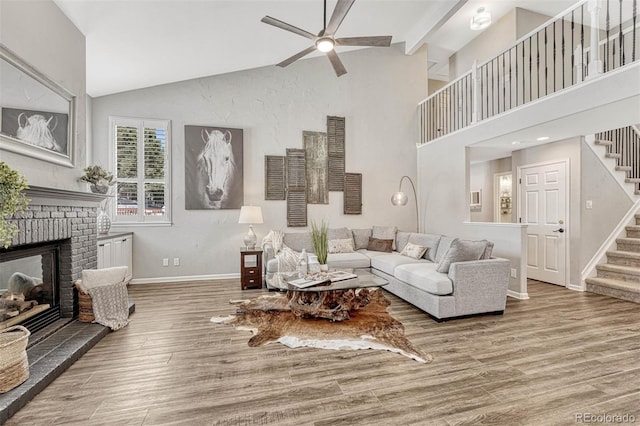 living room with beamed ceiling, wood-type flooring, ceiling fan, and a fireplace