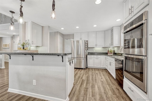 kitchen featuring appliances with stainless steel finishes, a kitchen bar, hanging light fixtures, light hardwood / wood-style floors, and white cabinets