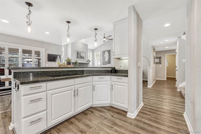 kitchen with white cabinets, kitchen peninsula, hanging light fixtures, black stovetop, and light wood-type flooring