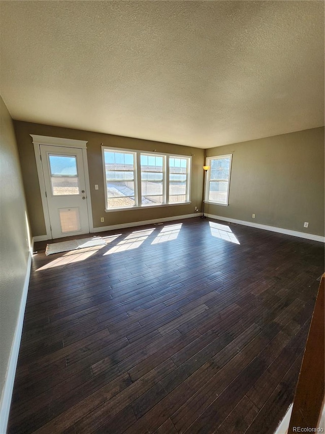 unfurnished living room with dark wood-type flooring, a textured ceiling, and baseboards