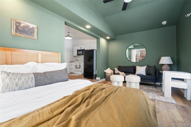 bedroom featuring lofted ceiling, light hardwood / wood-style flooring, black refrigerator, and ceiling fan