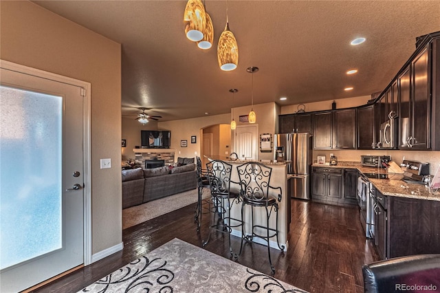 12420 Mount Belford Way, Peyton, CO 80831 - kitchen with appliances with stainless steel finishes, a fireplace, a breakfast bar area, dark brown cabinets, and dark wood finished floors