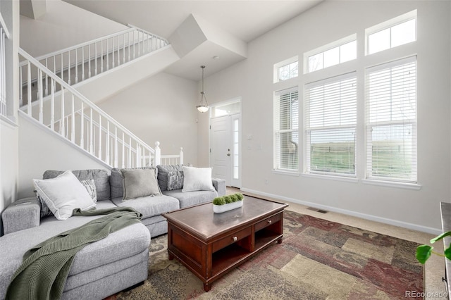 living area featuring visible vents, stairway, carpet flooring, a high ceiling, and baseboards