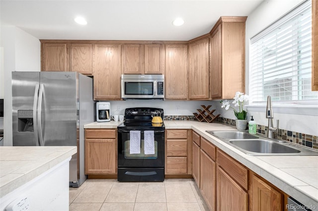 kitchen featuring tile countertops, recessed lighting, light tile patterned floors, a sink, and stainless steel appliances