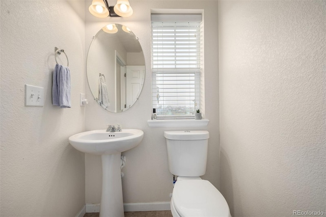 half bath featuring toilet, baseboards, and a sink